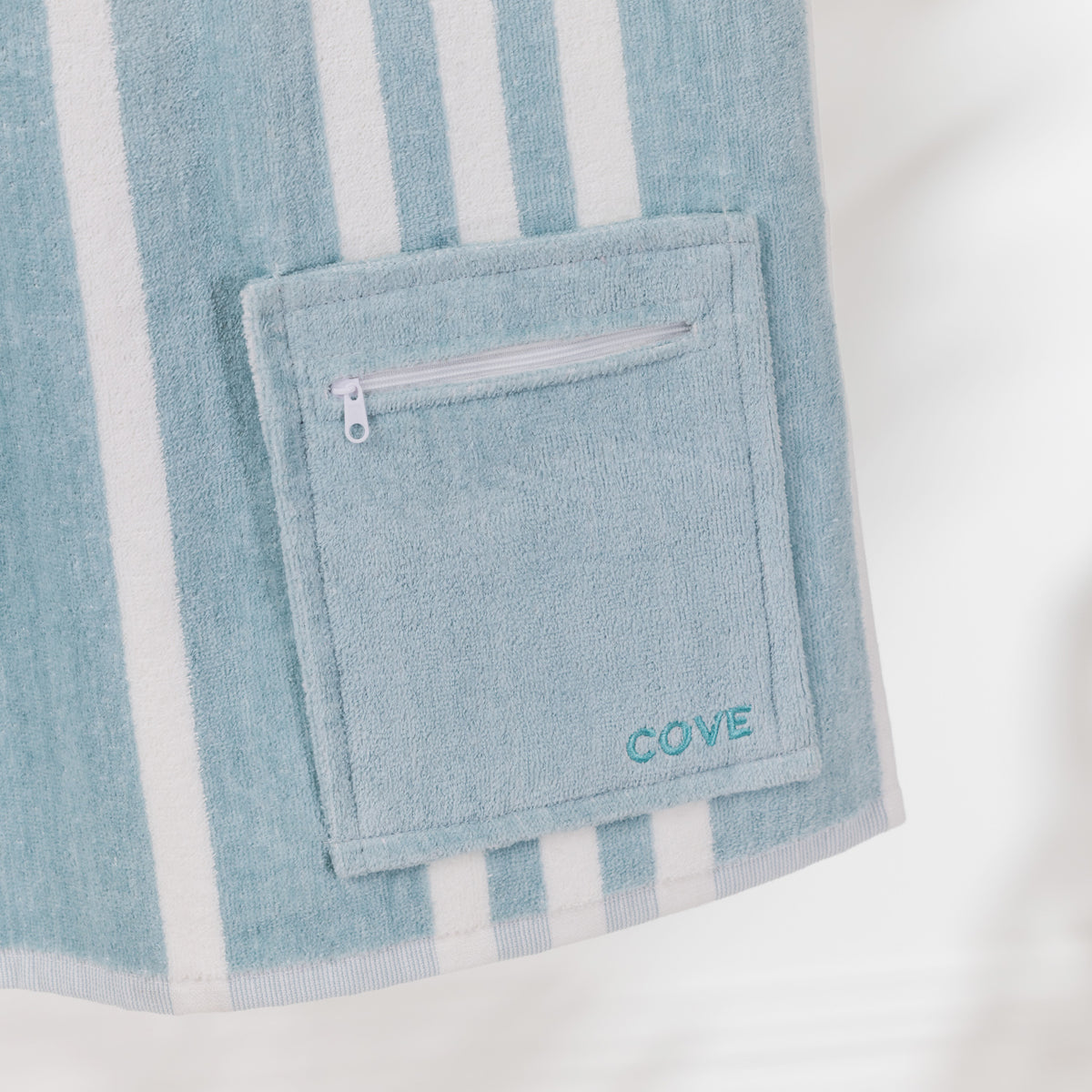 Close-up of the Seafoam Blue Cove Pocket Towel showing the matching zippered pocket, white stripe detailing and embroidered Cove logo.