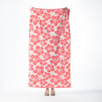 Pink beach towel featuring an all-over hibiscus floral pattern, held up against a white background.