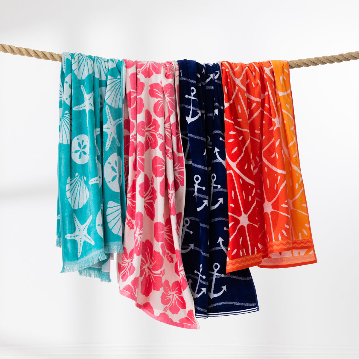 Colourful beach towel range in aqua, pink, navy, red and orange designs draped over a rope against a white background.