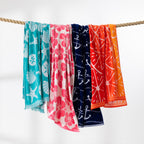 Colourful beach towel range in aqua, pink, navy, red and orange designs draped over a rope against a white background.