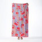 Pink beach towel featuring red cherries and blue vertical stripes, held up against a white background.