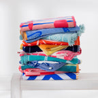 Colourful assortment of folded beach towels stacked on a white bench.