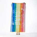 Multi-coloured striped beach towel featuring “SEA SUN SUMMER” text with playful summer-inspired motifs, held up against a white background.