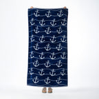 Navy blue beach towel featuring an all-over white anchor design with wavy stripe detailing, held up against a white background.