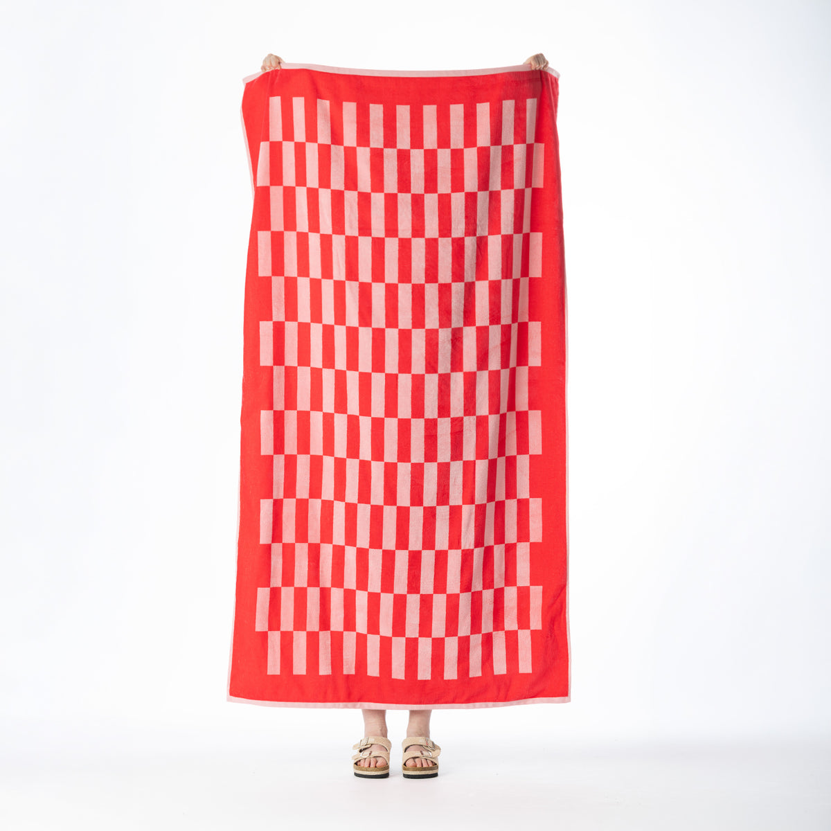 Red beach towel featuring a pale pink woven check pattern with a coordinating border, held up against a white background.