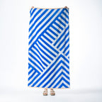 Blue and white beach towel featuring a bold geometric striped design with orange border detailing, held up against a white background.