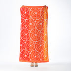 Orange beach towel featuring a bold citrus slice design with contrasting pale pink detailing and decorative borders, held up against a white background.