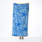 Blue beach towel featuring a bold starfish design in varying shades of blue with a contrasting orange border, held up against a white background.