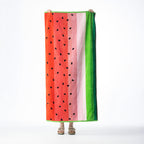 Watermelon-inspired beach towel featuring red, pink and green vertical stripes with black seed detailing, held up against a white background.