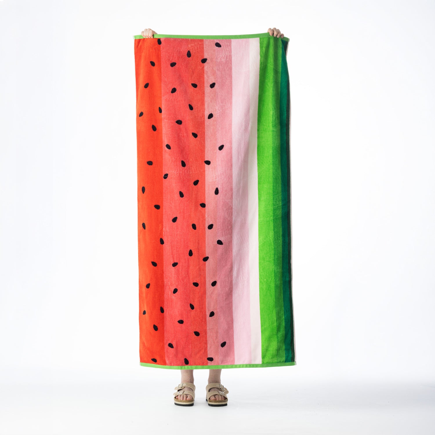 Watermelon-inspired beach towel featuring red, pink and green vertical stripes with black seed detailing, held up against a white background.