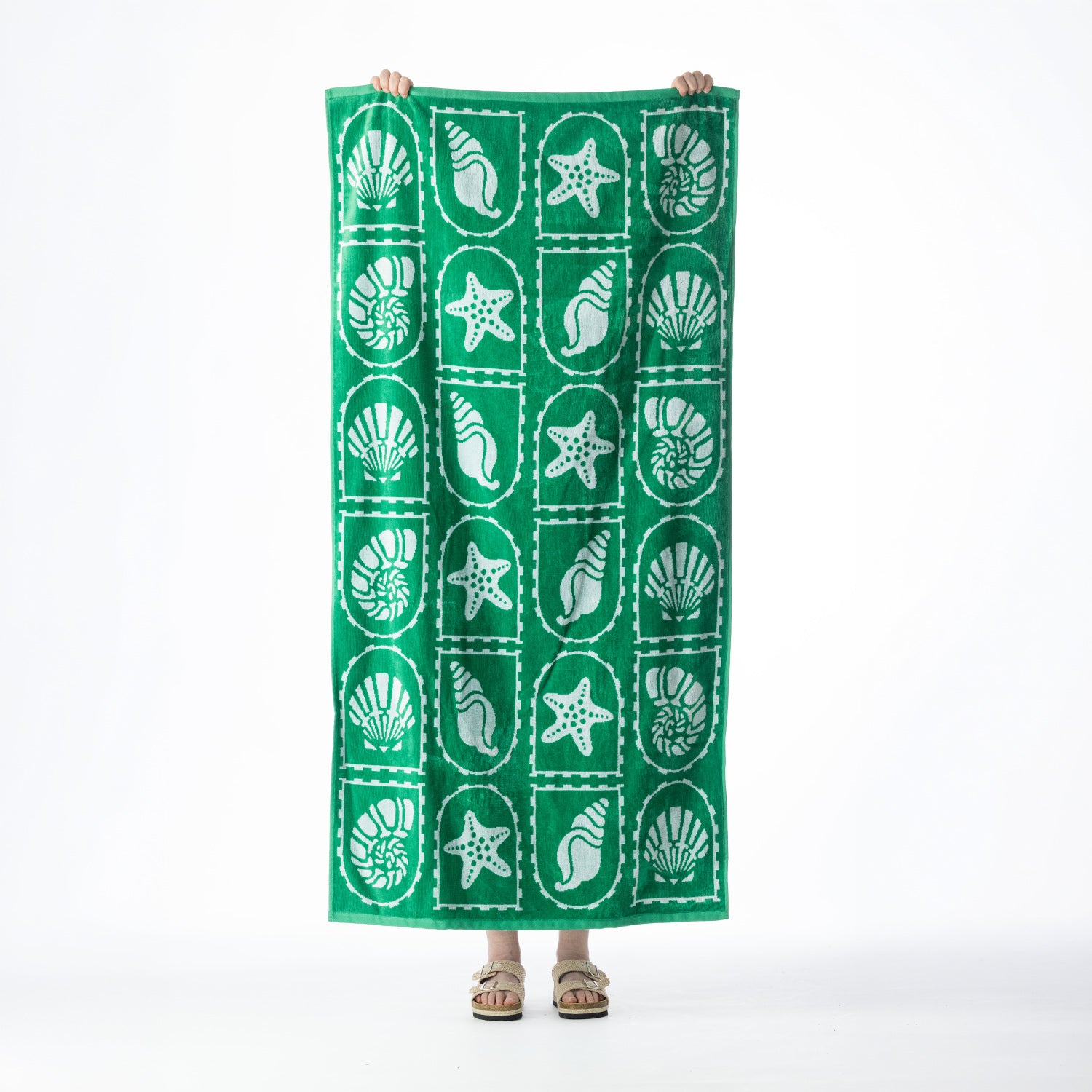 Green beach towel featuring a repeating white seashell and starfish design, held up against a white background.
