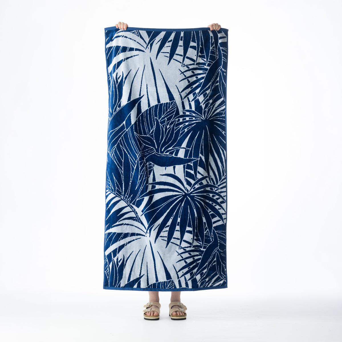 Navy blue beach towel featuring an all-over tropical palm leaf design in contrasting light blue, held up against a white background.