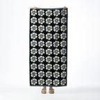 Black beach towel featuring a repeating cream floral design, held up against a white background.
