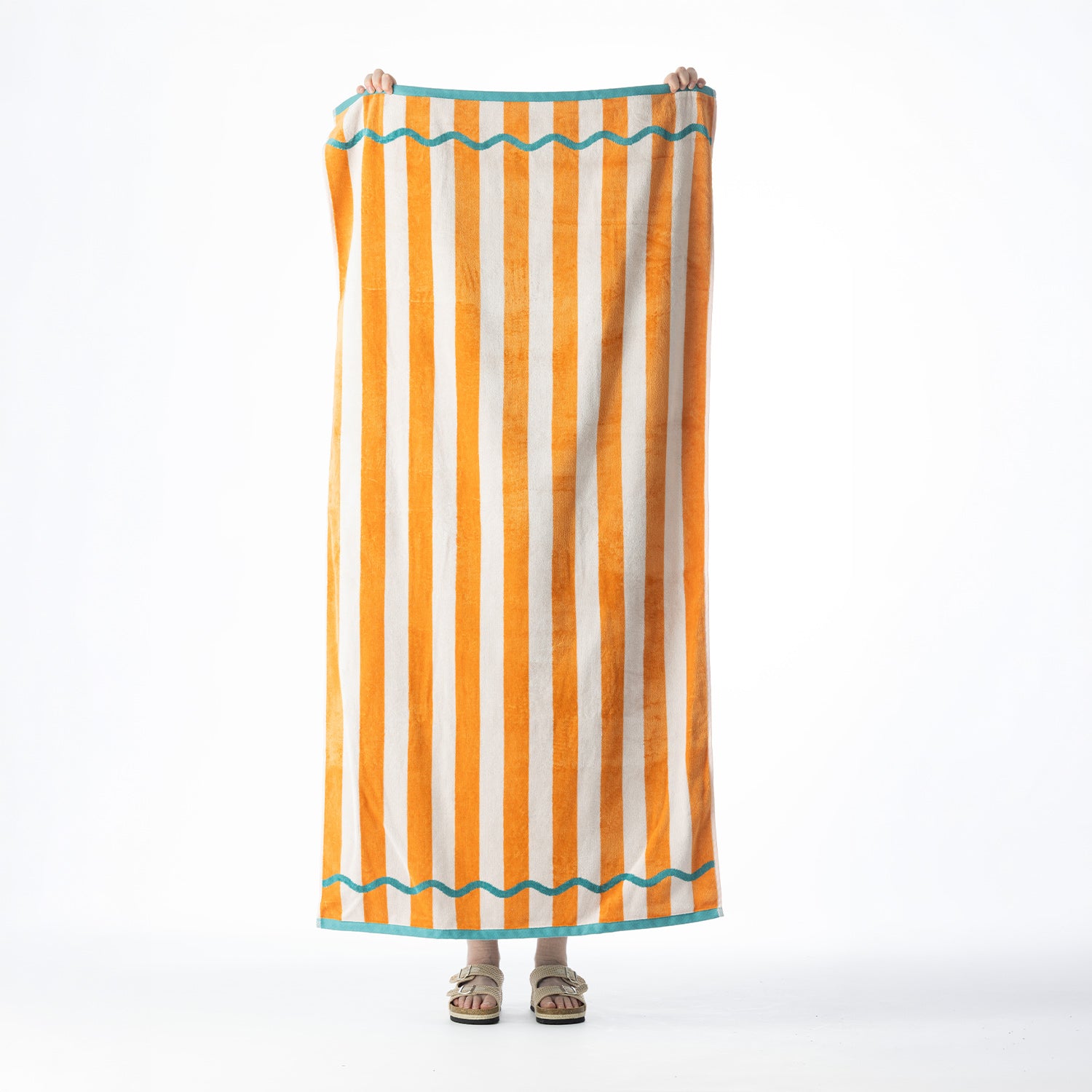 Orange and white striped beach towel with teal wavy line detailing and contrasting teal borders, held up against a white background.