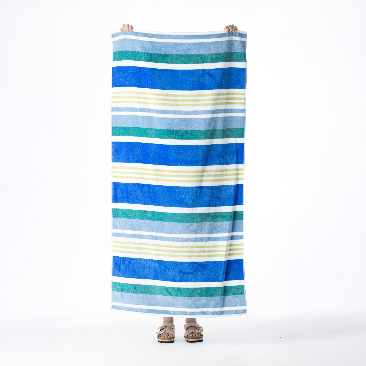 Multicoloured beach towel featuring horizontal stripes in blue, teal, light blue, white and pale green, held up against a white background.