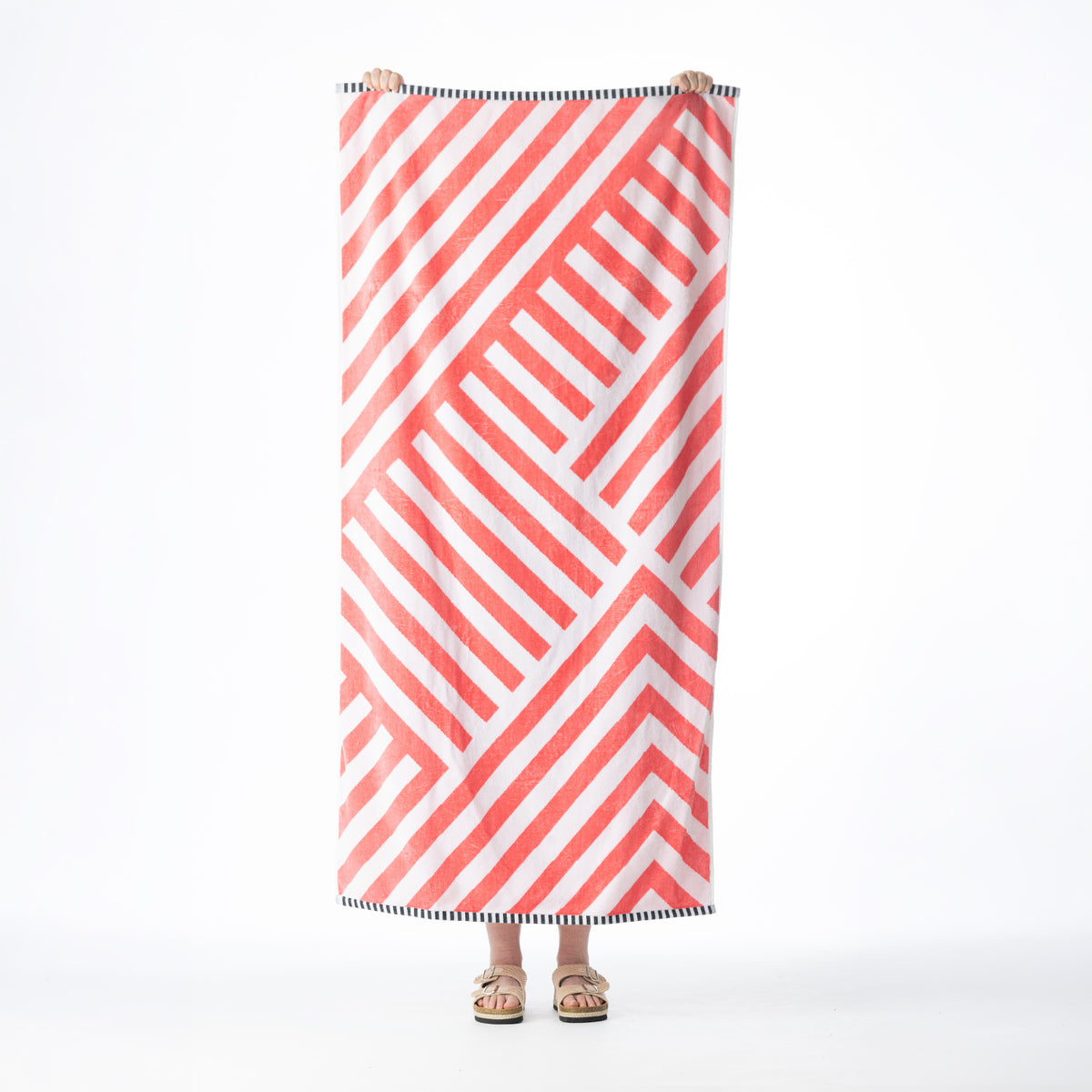 Orange and white beach towel featuring a bold geometric stripe design with contrasting black and white striped borders, held up against a white background.