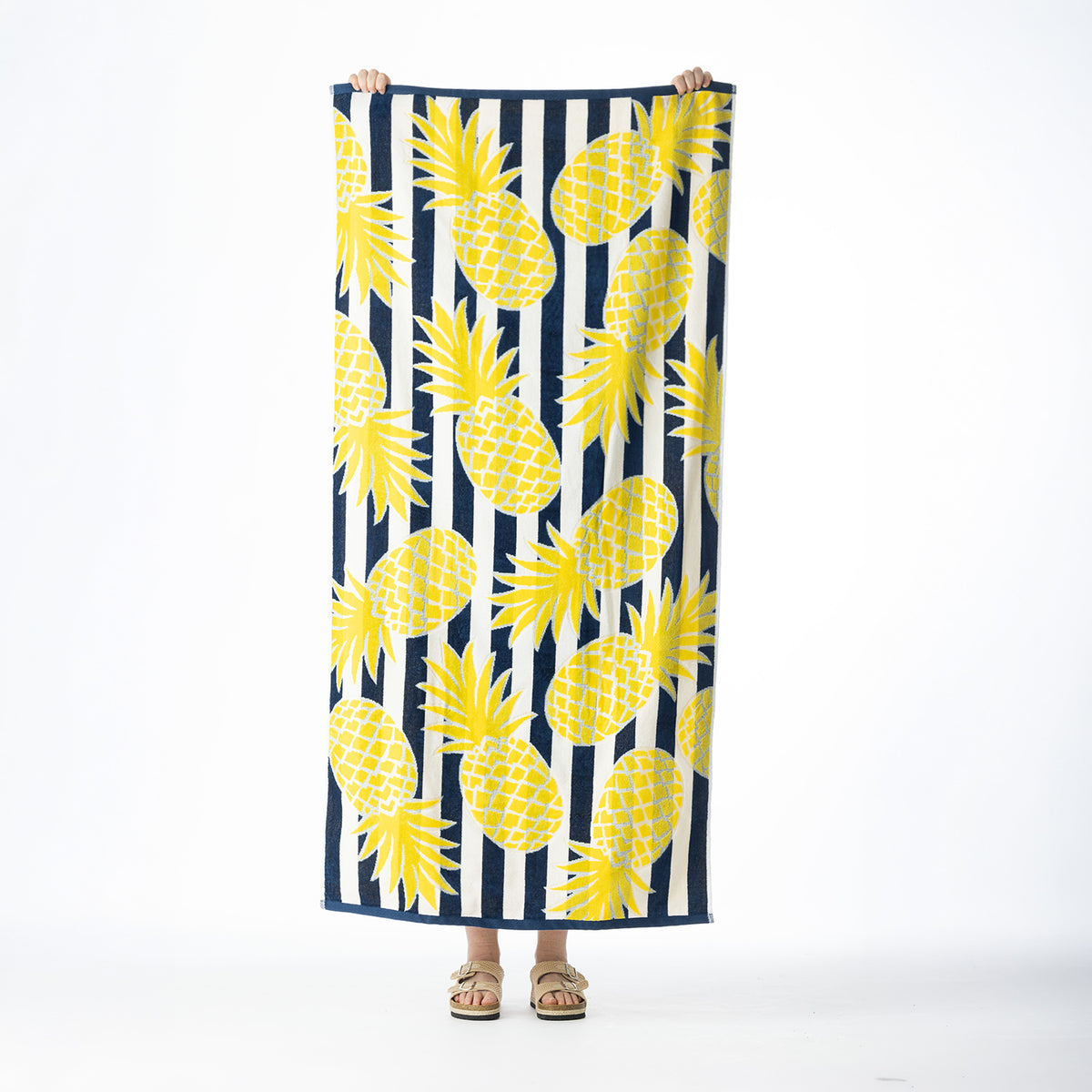 Navy and white striped beach towel featuring a bold yellow pineapple design, held up against a white background.