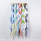 Six striped beach towels in assorted colors hang from a wooden rack against a plain white wall.