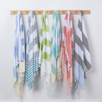 Six striped beach towels in assorted colors hang from a wooden rack against a plain white wall.