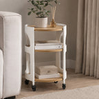 Solace Parker 3 Tier Trolley in white and natural styled beside a sofa, with a plant and diffuser on the top shelf, books on the middle shelf and a decorative box below. 