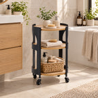 Solace Parker 3 Tier Trolley in Black/Natural displayed in a warm modern bathroom, styled with folded towels, bathroom accessories, a woven storage basket and potted greenery.