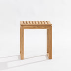 A small wooden stool with a slatted seat and blocky legs, shown on a clean white studio background.