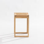 A minimalist wooden side table or stool with a light oak finish, featuring a slatted top and open geometric frame, photographed on a clean white studio background.