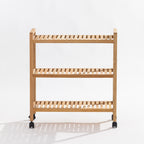 A three-tier wooden rolling shelf cart with a light natural oak finish and black caster wheels, photographed against a clean white studio background.