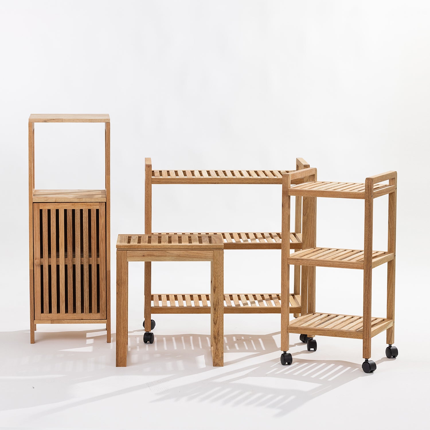 A set of four light natural wood Bathroom furniture pieces, including two rolling storage shelves on casters, a small table, and a tall narrow cabinet, photographed on a clean white studio background.