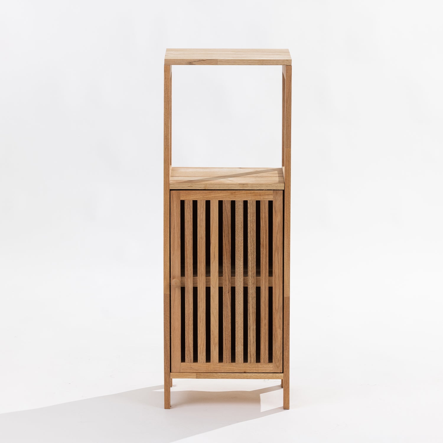 A tall, minimalist wooden storage cabinet with an open top shelf and a lower slatted door, shown against a plain white studio background.