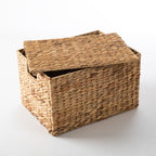 Natural water hyacinth woven cube storage basket with a matching fitted lid, shown partially open with integrated cut-out side handles.