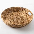 Round natural water hyacinth woven tray with integrated side handles and a braided textured finish.