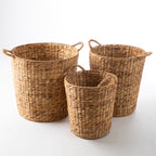 Set of three natural water hyacinth woven storage baskets with integrated side handles in assorted sizes.