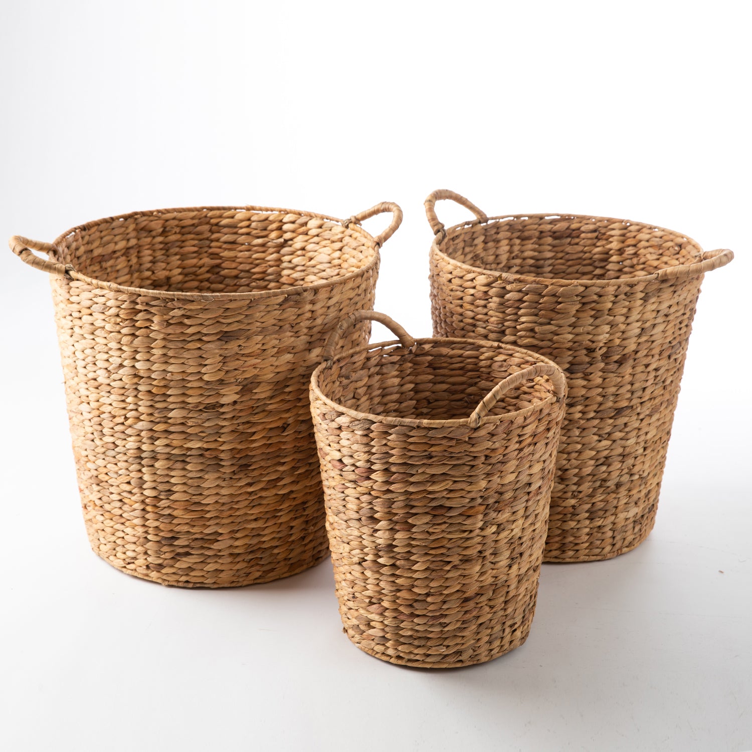 Set of three natural water hyacinth woven storage baskets with integrated side handles in assorted sizes.
