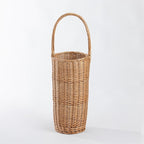 A tall, cylindrical woven wicker basket with a single arched handle, shown on a clean white studio background.