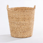 A natural woven seagrass or straw storage basket with integrated side handles, shown on a clean white studio background.