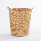 A natural woven straw basket with two loop handles, shown on a clean white background.