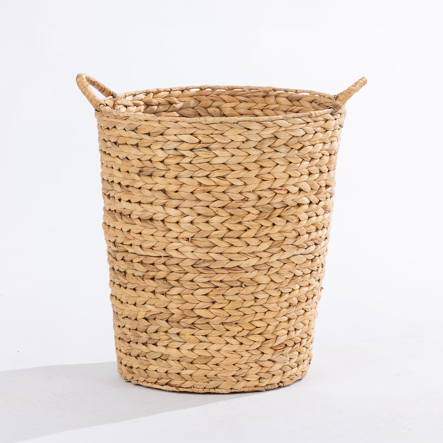 A natural woven straw basket with two loop handles, shown on a clean white background.