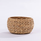 A round, hand-woven basket made from natural straw or seagrass, shown on a clean white background.