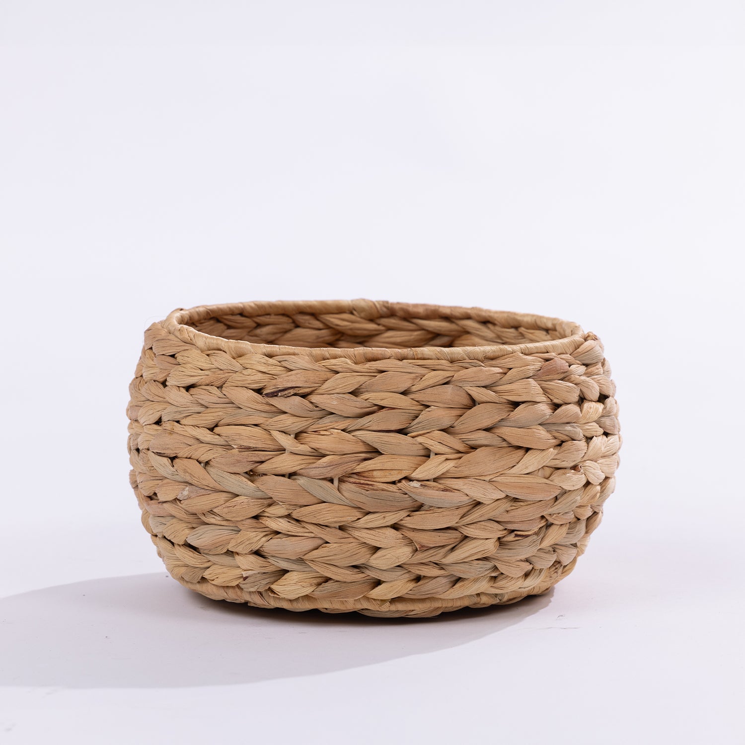 A round, hand-woven basket made from natural straw or seagrass, shown on a clean white background.