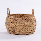 A round woven basket made from natural straw or seagrass with two loop handles, shown on a clean white background.