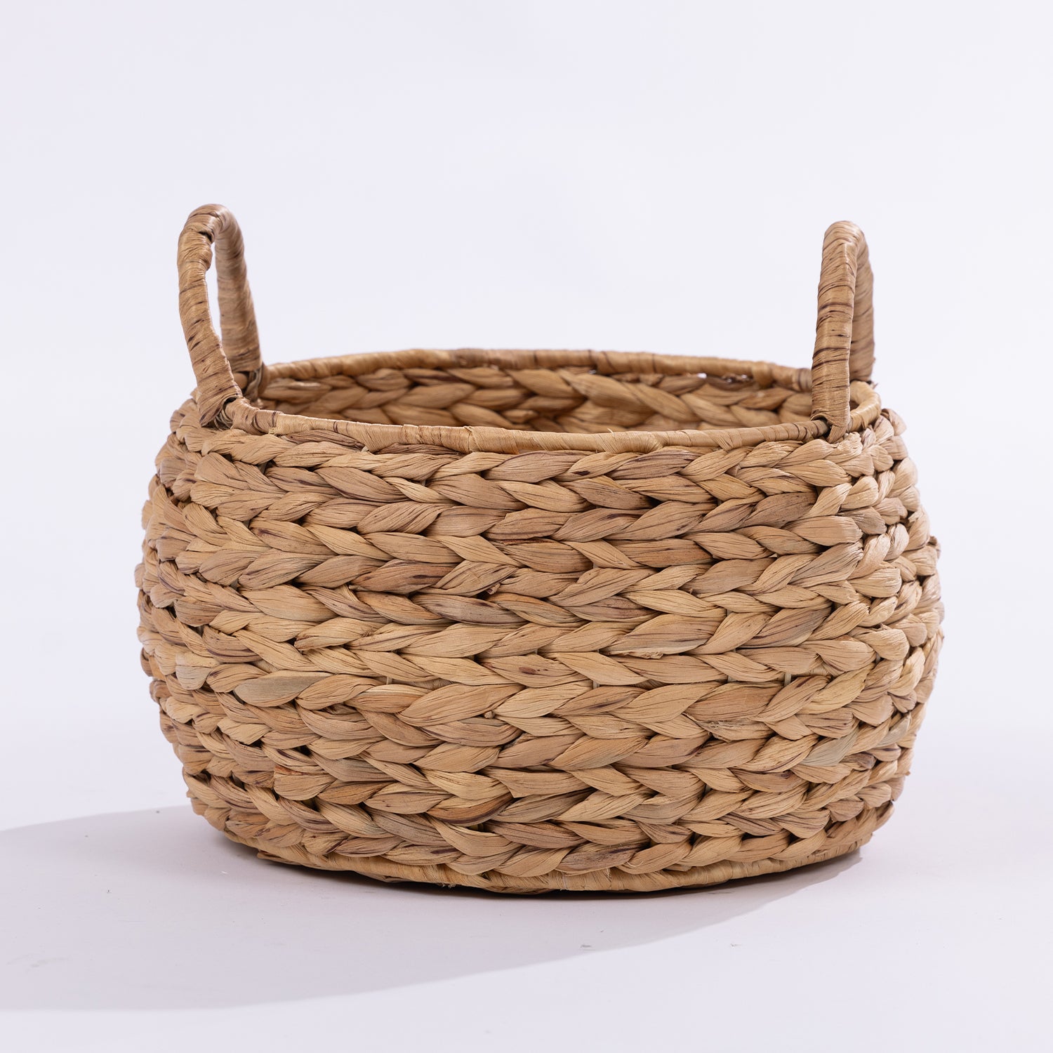 A round woven basket made from natural straw or seagrass with two loop handles, shown on a clean white background.