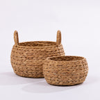 Two round woven seagrass baskets with loop handles, one larger and one smaller, displayed on a clean white studio background.