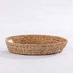 A round woven natural fiber basket with a shallow depth and integrated side handles, shown on a clean white background.