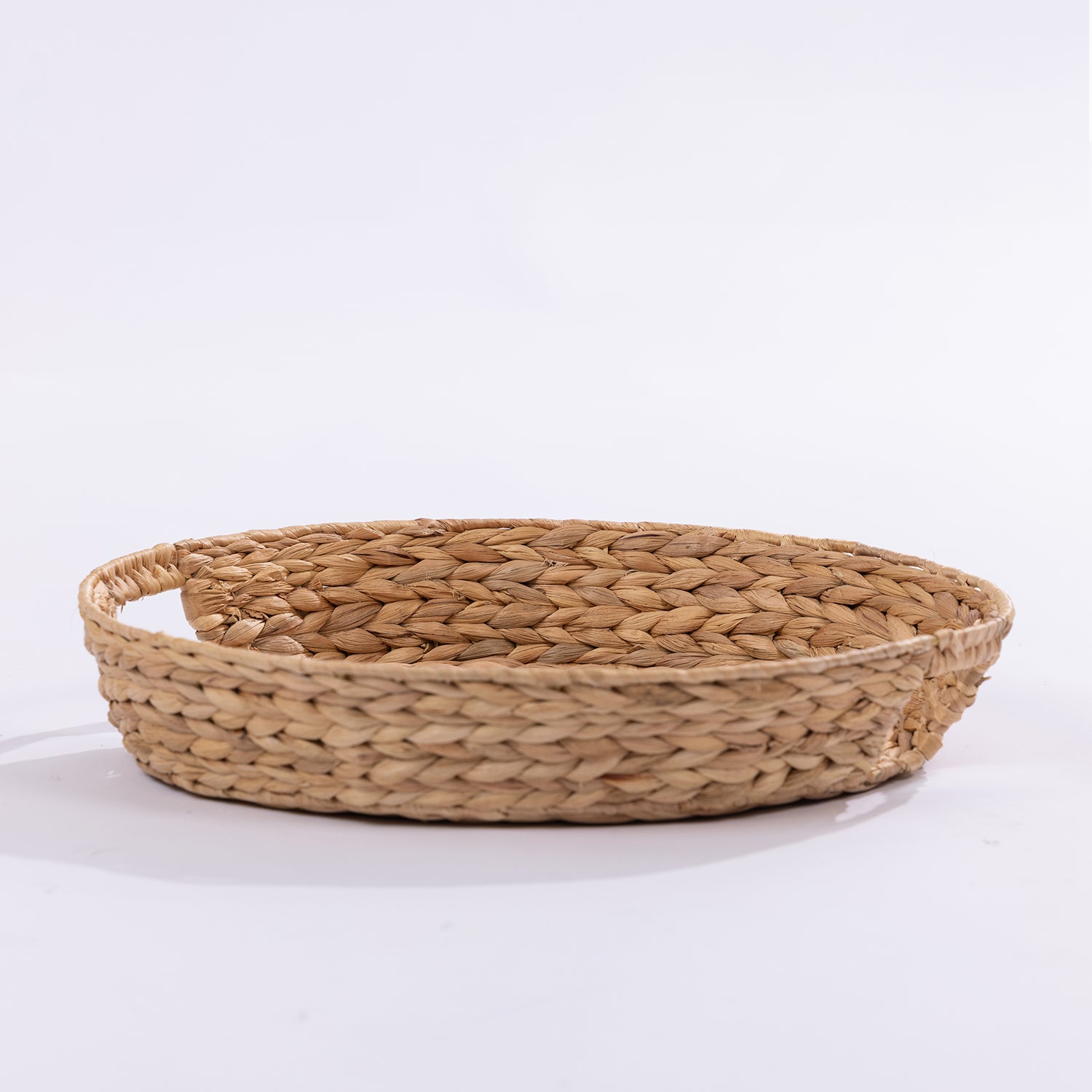 A round woven natural fiber basket with a shallow depth and integrated side handles, shown on a clean white background.