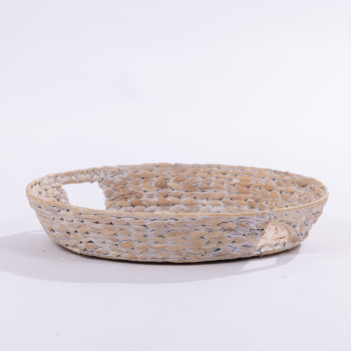 A shallow round woven tray made from natural straw or seagrass with a single integrated handle, shown on a clean white studio background.