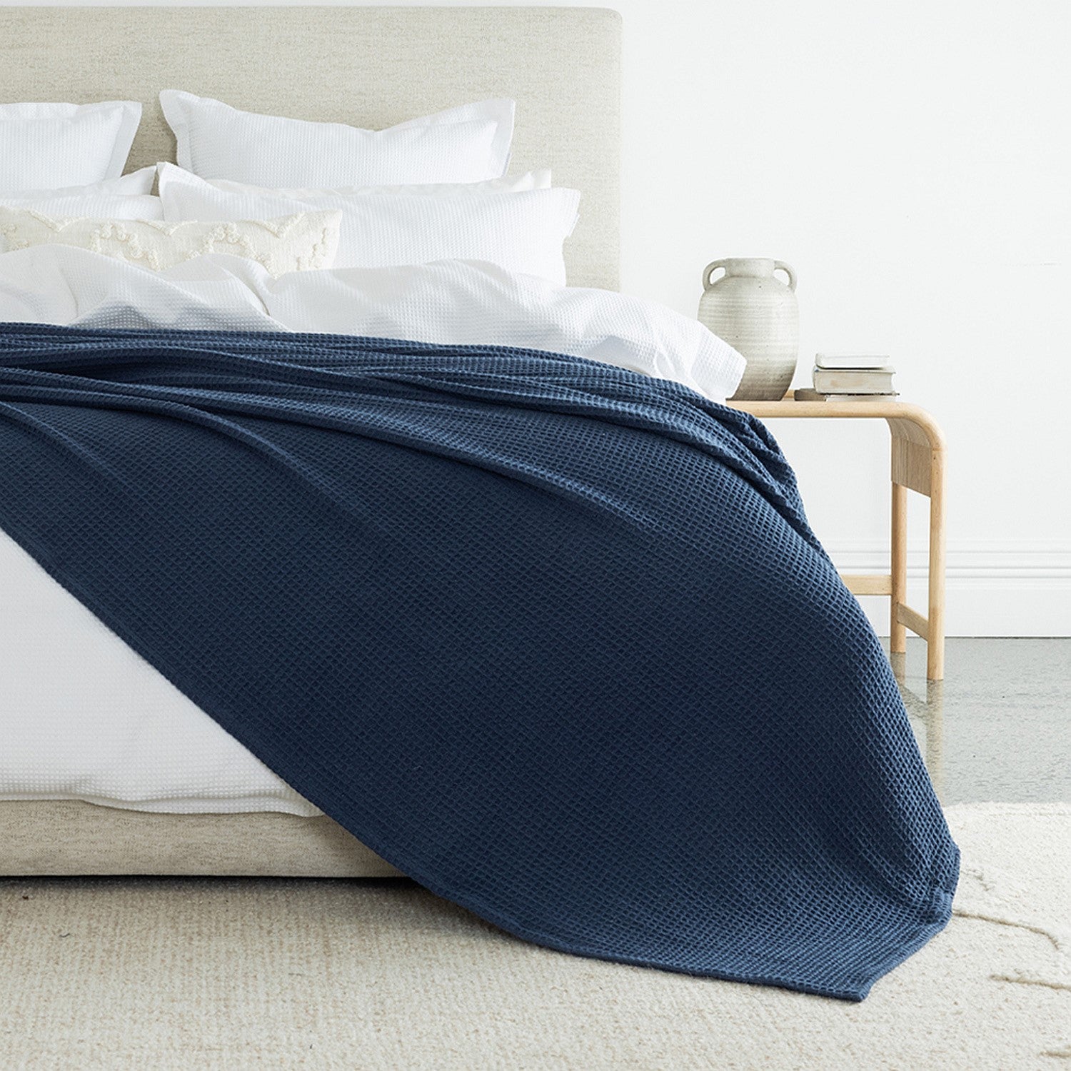 A richly textured blue waffle-weave blanket draped across crisp white bedding adds depth, warmth, and timeless elegance to the bedroom.