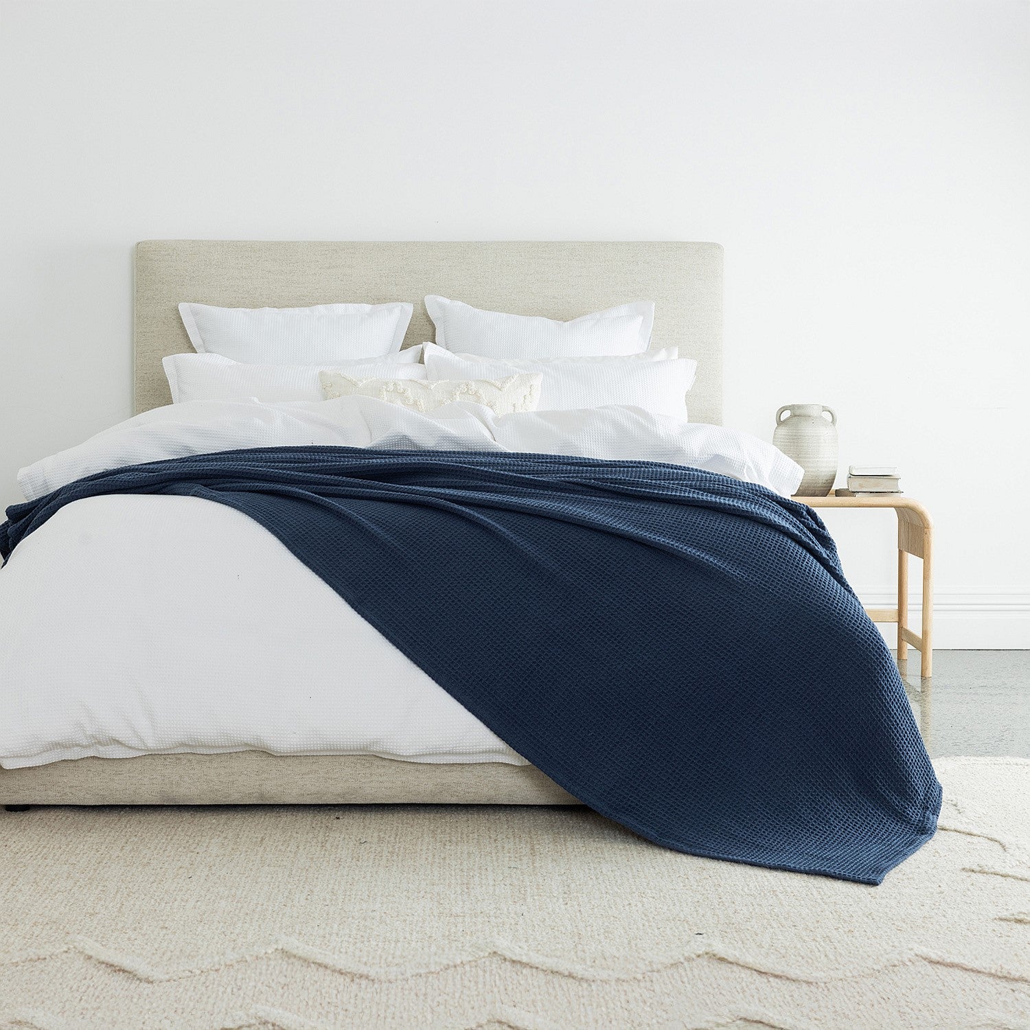 A richly textured blue waffle-weave blanket draped across crisp white bedding adds depth, warmth, and timeless elegance to the bedroom.