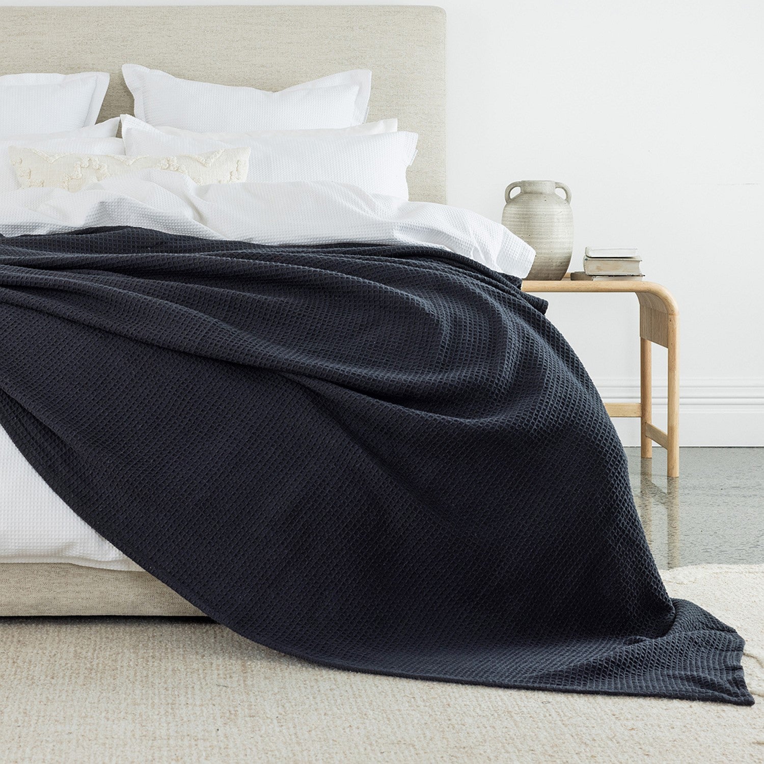 A richly textured coal waffle-weave blanket draped across crisp white bedding adds depth, warmth, and timeless elegance to the bedroom.