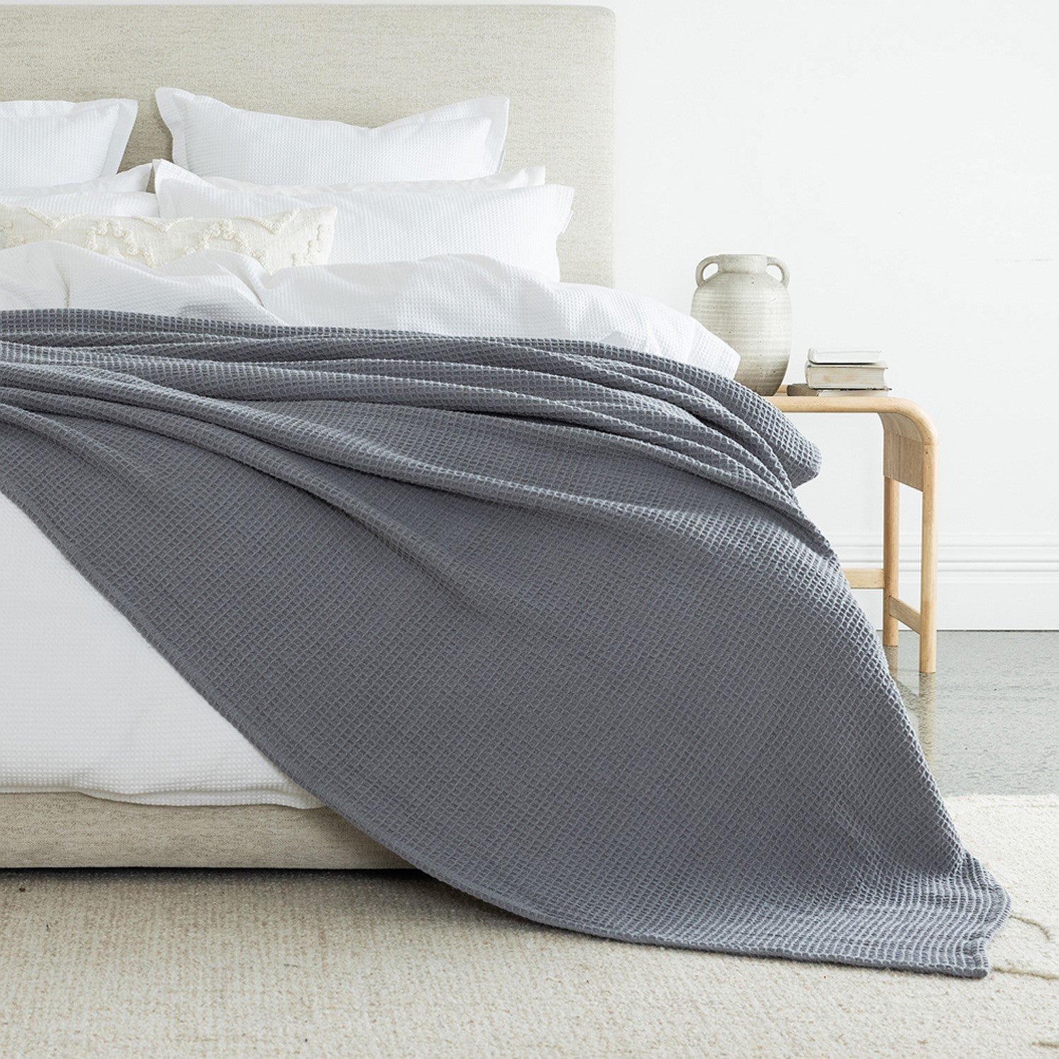 A richly textured grey waffle-weave blanket draped across crisp white bedding adds depth, warmth, and timeless elegance to the bedroom.